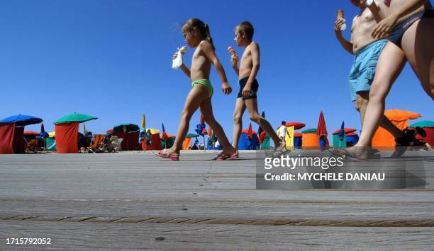 Des vacanciers marchent, une glace à la main, le 04 août 2007 sur les planches de la plage de Deauville, où le week-end s'annonce ensoleillé. Les...