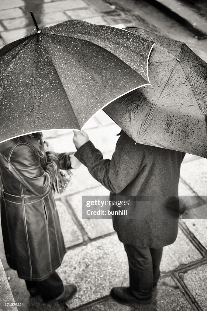Unidentifiable couple s'abriter de la pluie sous des parasols