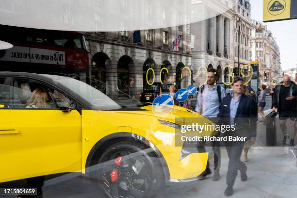 Reflections of passers-by and potential buyers looking at a Lotus 'Eletre' EV car which is positioned in the window of the brand's showroom on...