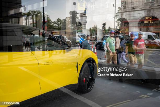 Reflections of passers-by and potential buyers looking at a Lotus 'Eletre' EV car which is positioned in the window of the brand's showroom on...