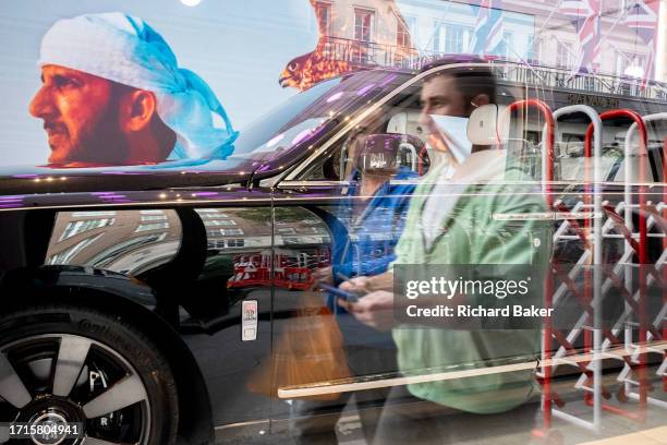 Members of the public walk past the window of the Rolls-Royce car showroom in Mayfair where a 'Ghost' model is displayed in the dealership's window,...