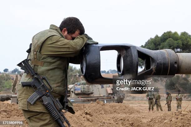 An Israeli soldier rests his head on the gun barrel of a self-propelled artillery howitzer as Israeli soldiers take positions near the border with...