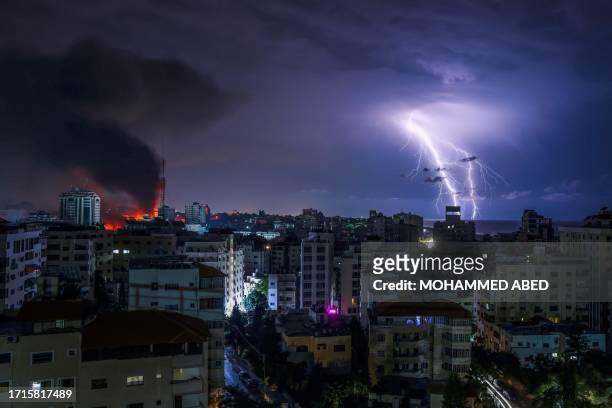 Lightning strikes as smoke billows following an Israeli airstrike in Gaza City on October 9, 2023. One month after Israel was wracked by Hamas...