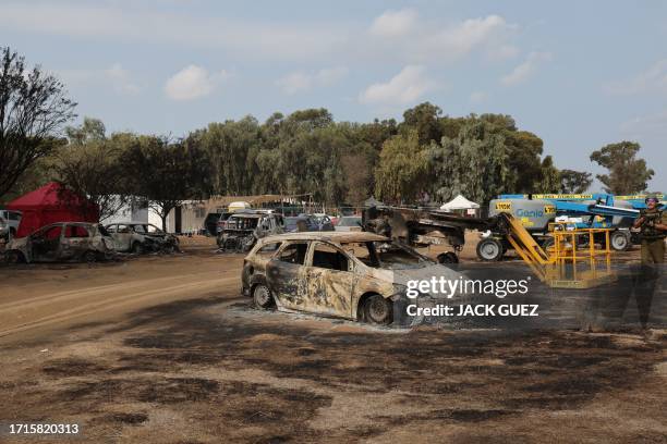 An Israeli soldier walks past burnt vehicles at the site of the weekend attack on the Supernova desert music Festival by Palestinian militants near...