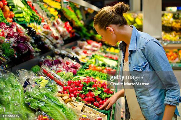 a young woman looking at fresh vegetables in the supermarket - arm made of vegetables stockfoto's en -beelden