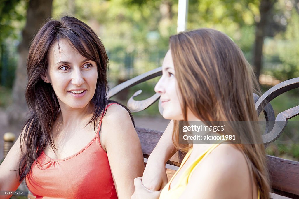 Mother and daughter sitting on bench in the park outdoors.