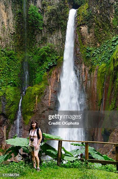 woman standing in front of towering tropical waterfall - ogphoto and costa rica stock pictures, royalty-free photos & images