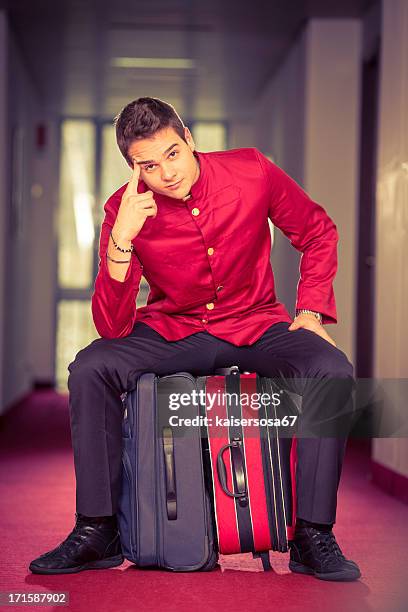 bell boy sitting on suitcase - bellhop stock pictures, royalty-free photos & images