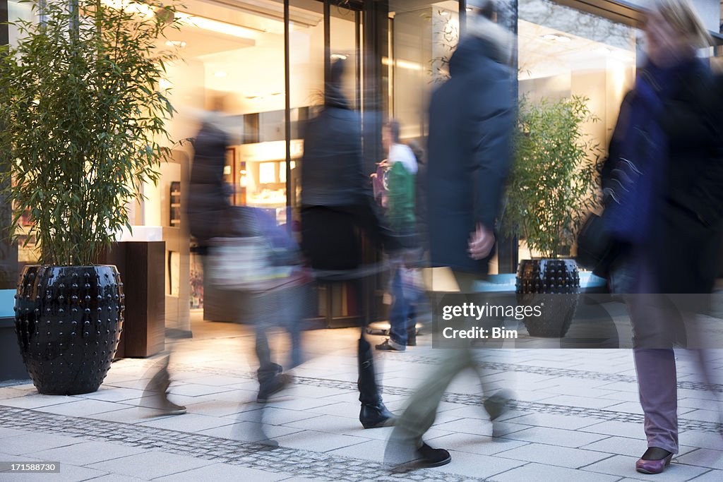 Blurred People Walking Past Illuminated Fashion Store