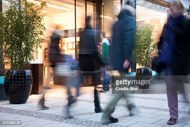 blurred people walking past illuminated fashion store - silhouette münchen stock pictures, royalty-free photos & images