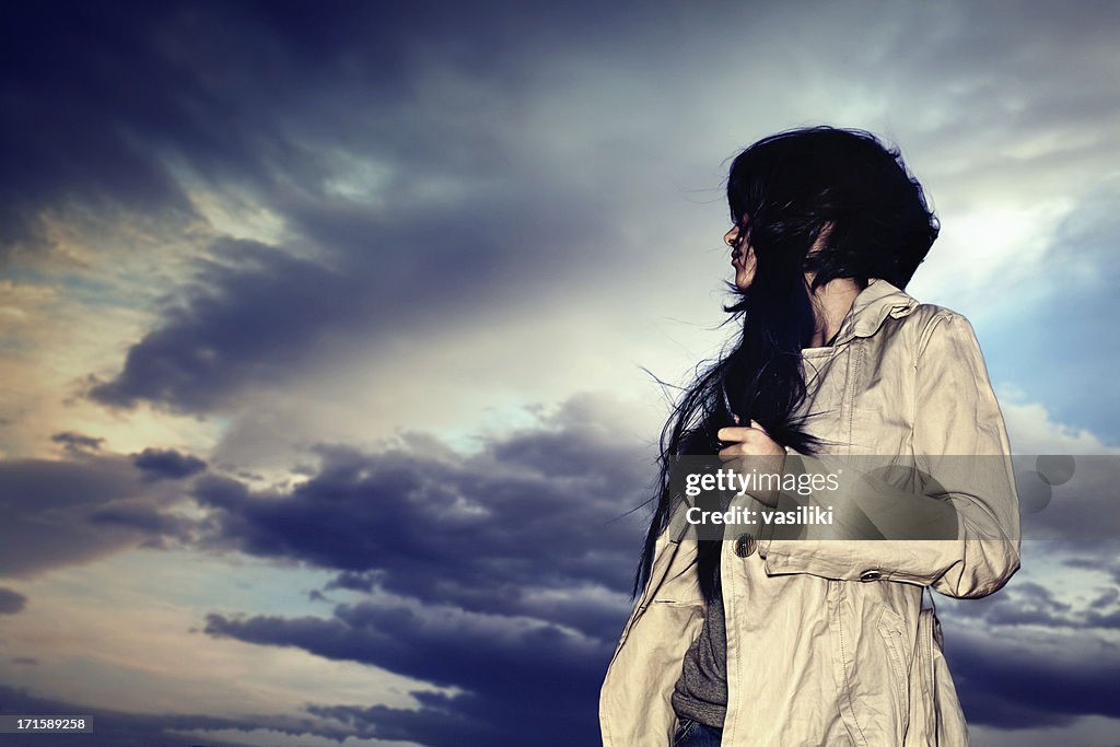 Jeune femme avec un trench-coat contre un ciel Sombre et mélancolique
