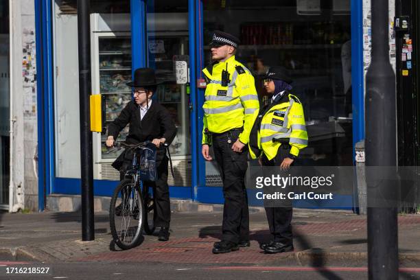 An Orthodox Jewish boy waits to cross a road next to police officers patrolling Stamford Hill, an area of London with a large Jewish community, on...