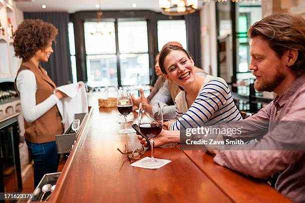 woman and man at bar chatting and checking cell phone - bar man t shirt stock-fotos und bilder