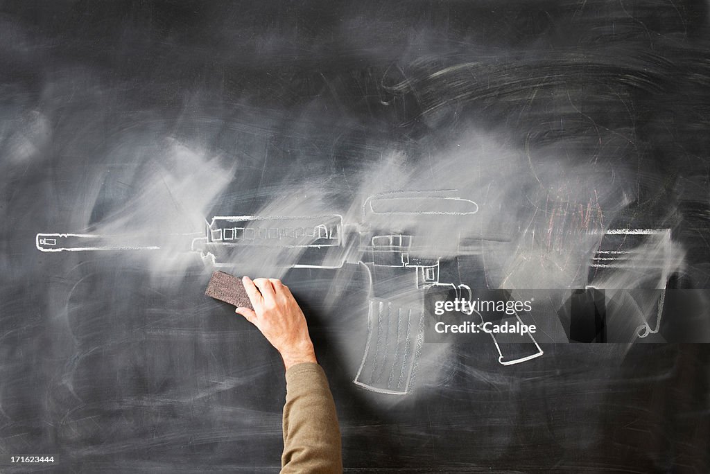 Person erasing chalk drawing of gun on blackboard