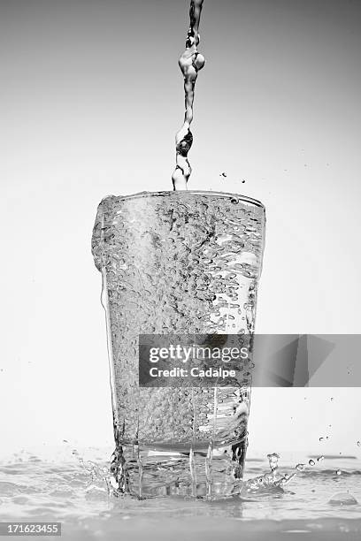 water being poured into drinking glass and overflowing - overflowing glass stockfoto's en -beelden