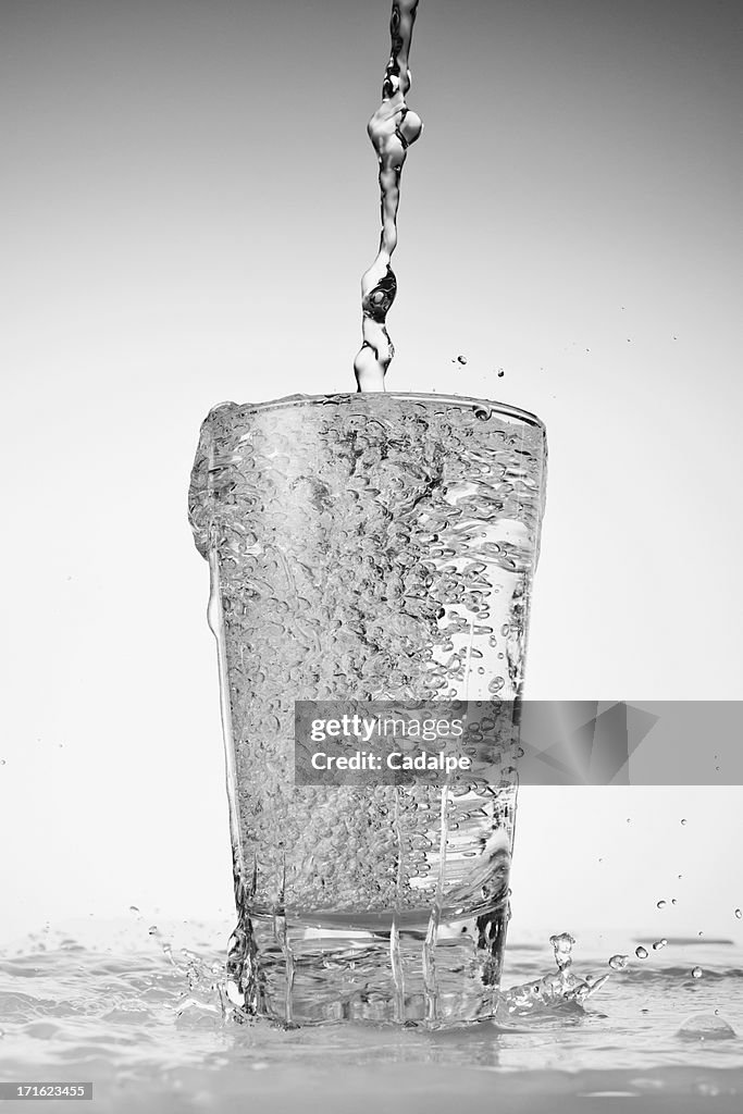 Water being poured into drinking glass and overflowing