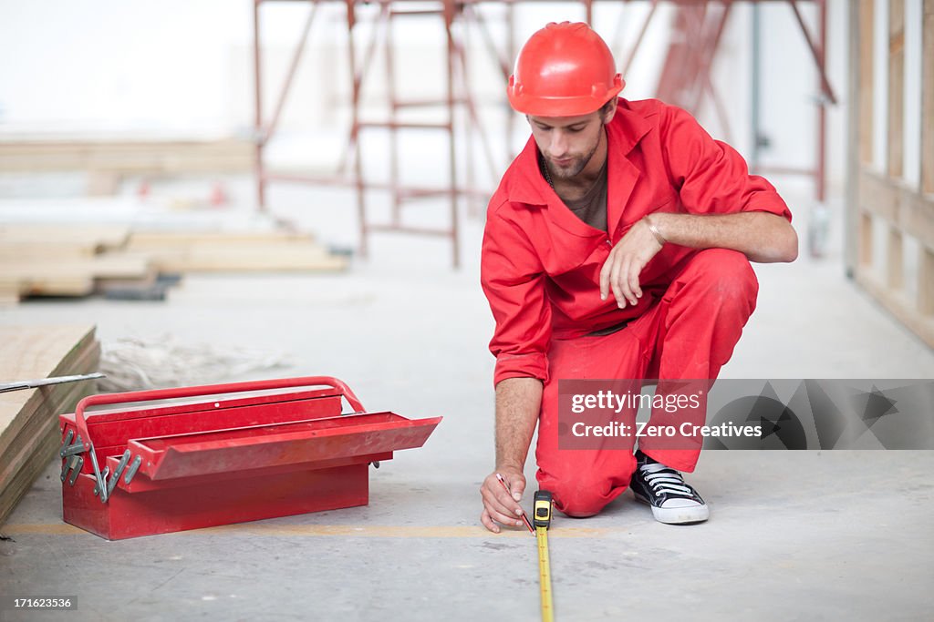 Builder with tool box and pencil measuring floor on construction site