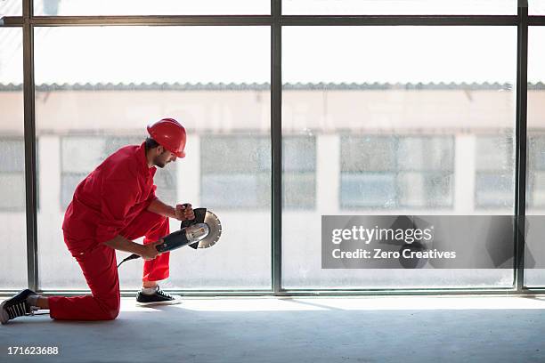 laborer kneeling in front of window with circular saw - red jumpsuit stock pictures, royalty-free photos & images
