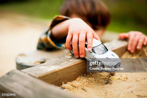 male toddler holding toy car above sandpit - toy car stock pictures, royalty-free photos & images