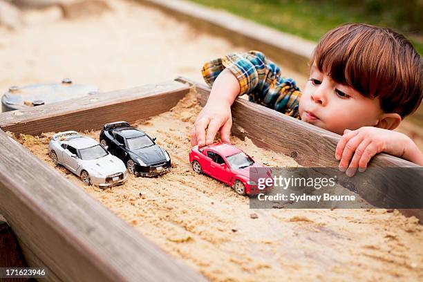 male toddler reaching to play with toy cars in sandpit - 2 boys 1 sandbox stock pictures, royalty-free photos & images