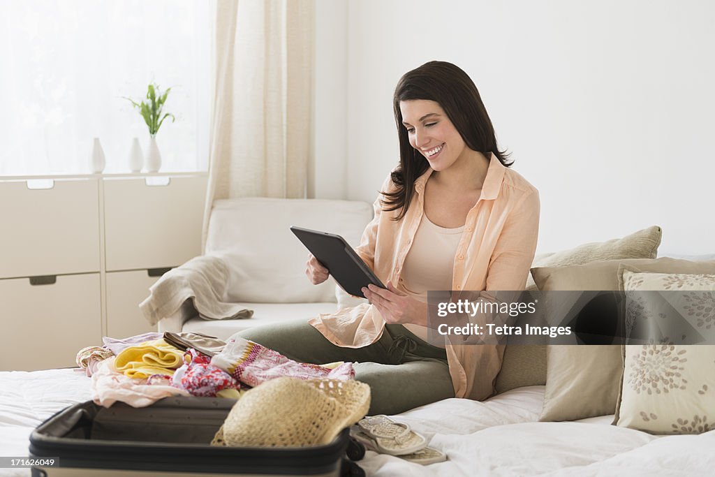 USA, New Jersey, Jersey City, Woman using digital tablet while packing suitcase