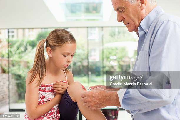 grandfather putting bandage on granddaughters knee - scraped knee stock pictures, royalty-free photos & images