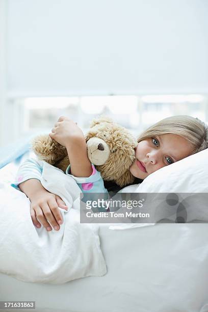 sick girl laying in bed with teddy bear - teddy day stockfoto's en -beelden