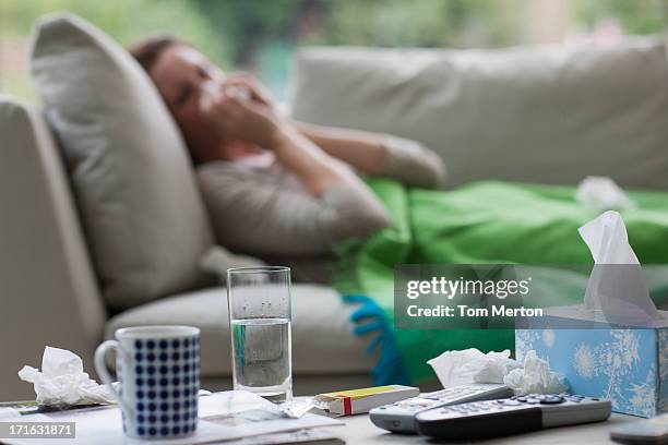 sick woman laying on sofa blowing nose - ziekte stockfoto's en -beelden