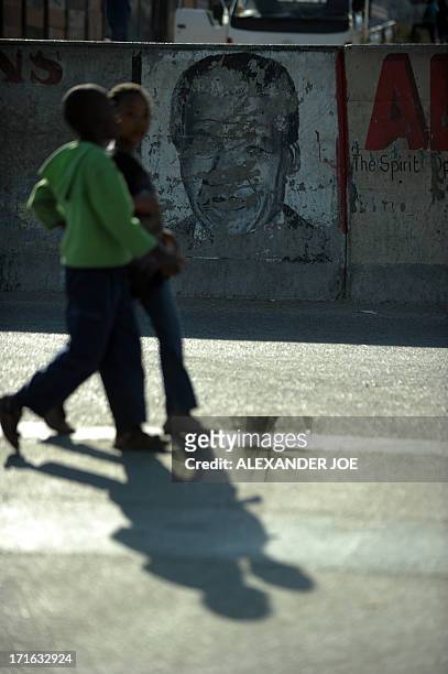 Alexandra children walk past an old painiting of Nelson Mandela on the street of Alexandra township on June 27, 2013. Mandela is spending his 20 day...