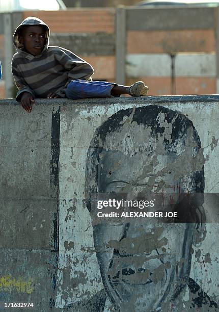 Child sits on a wall with an old painting of Nelson Mandela on a street of Alexandra township on June 27, 2013. Mandela is spending his 20 day in the...