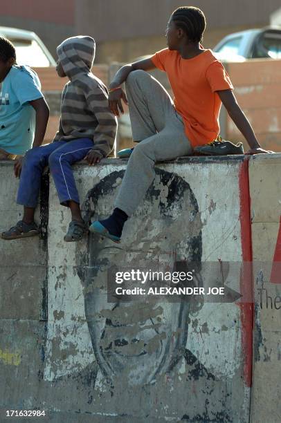 Children sit on a wall with an old painting of Nelson Mandela on a street of Alexandra township on June 27, 2013. Mandela is spending his 20 day in...