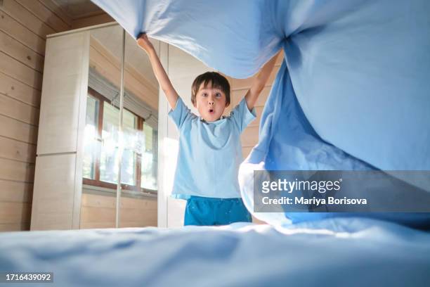 a boy in a blue t-shirt is making his bed. - children room stock pictures, royalty-free photos & images