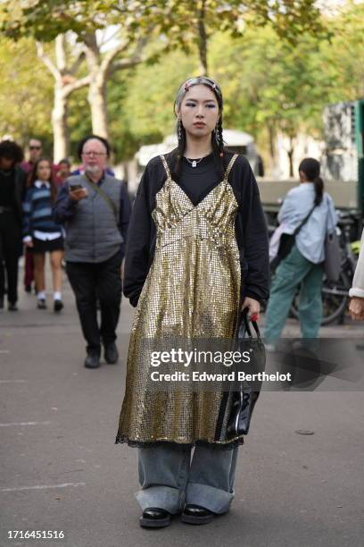 Guest wears hair clips, a black sweater, a necklace, a golden shiny sequined dress, a violin shaped bag, blue denim jeans / pants, black shoes,...