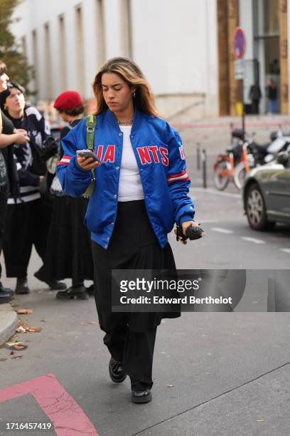 Guest wears a blue bomber jacket, a white t-shirt, a black pleated skirt, black shoes, a green bag, during the Womenswear Spring/Summer 2024 as part...