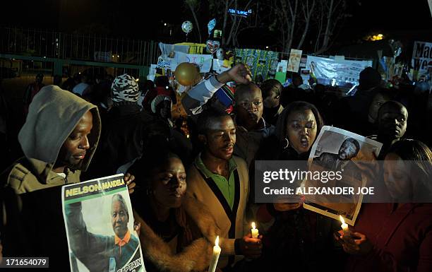 Group of well-wishers hold candles and photos of Nelson Mandela as they pray for his recovery outside the Mediclinic heart hospital where he is...