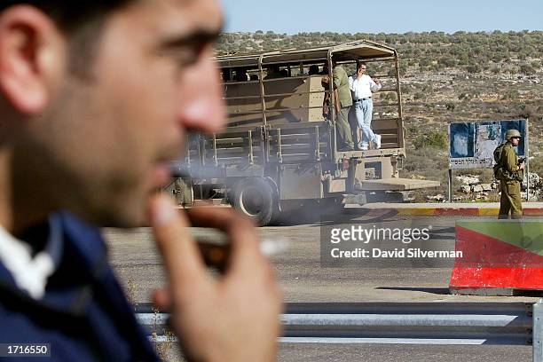 Palestinian smokes while waiting to get his documents checked as others standing in an army troop transporter are guarded by an Israeli soldier ater...