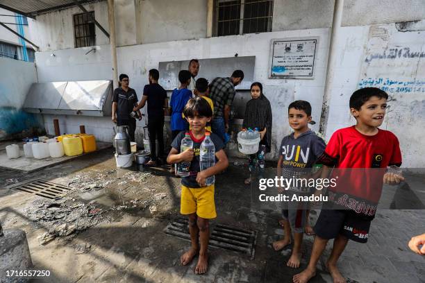 Children carry boxes filled with clean water from a dispenser as water shortage happens following the suspension of water flow from Israel to Gaza,...