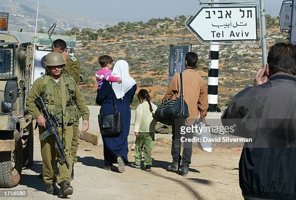 Palestinians and Israeli soldiers pass each other January 9, 2003 at the Israeli army roadblock at Tapuah Junction near the West Bank town of Nablus....
