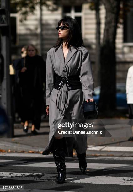 Guest is seen wearing a gray trench coat, black and silver belt, black boots and black sunglasses outside the Miu Miu show during the Womenswear...