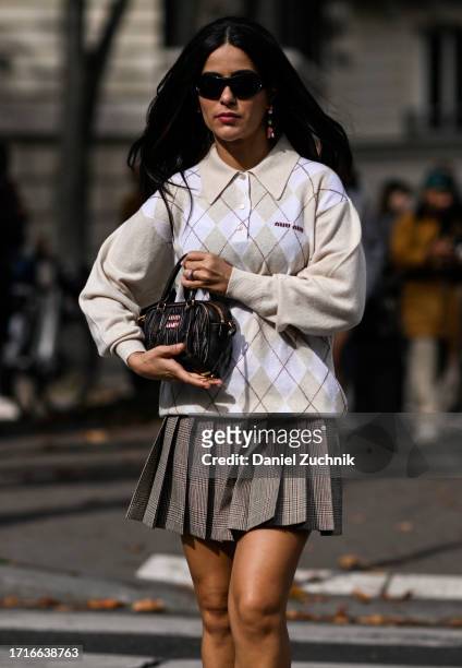 Mer is seen wearing a Miu Miu sweater, tan pleated skirt and black Miu Miu bag and black sunglasses outside the Miu Miu show during the Womenswear...
