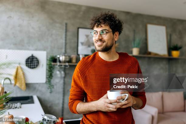 young man enjoying a cup of coffee in his domestic kitchen - wegkijken stockfoto's en -beelden