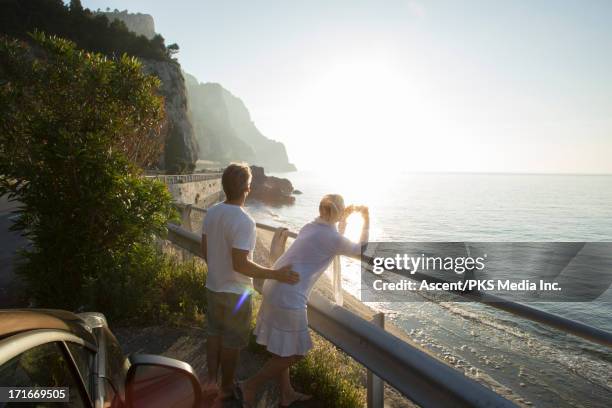 couple take picture by car, along coastal road - couple on the beach with car stockfoto's en -beelden