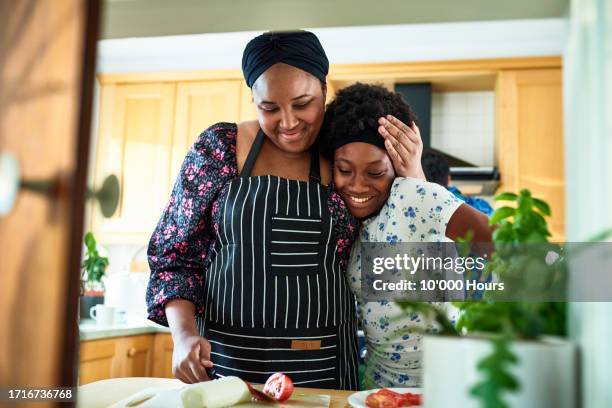 affectionate mid adult woman with arm around transgender girl in kitchen - tante photos photos et images de collection