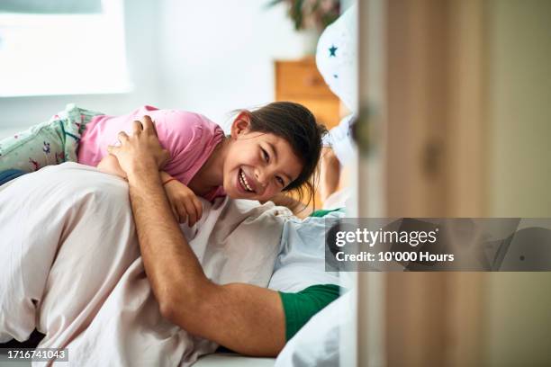 little girl lying on her dad in bed and giggling - human arm stock pictures, royalty-free photos & images