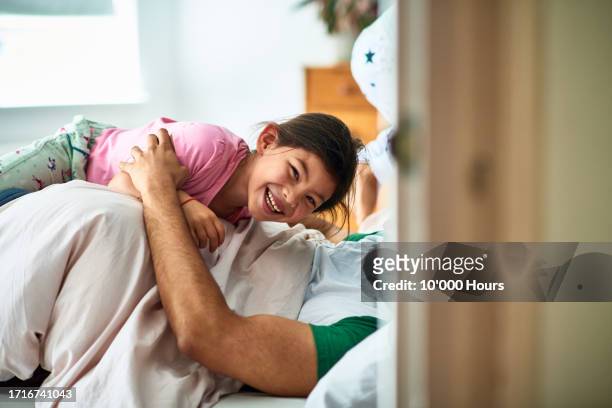 little girl lying on her dad in bed and giggling - cócegas imagens e fotografias de stock