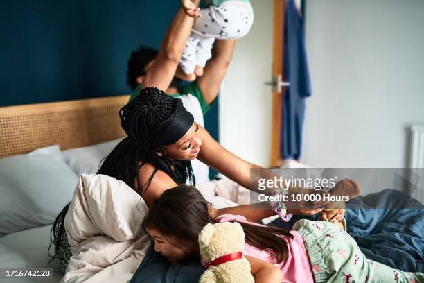 mother laughing and tickling girl on bed, father lifting son - male feet pics stock pictures, royalty-free photos & images