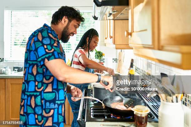 mid adult couple making dinner, man using frying pan - woman 30s house busy stock pictures, royalty-free photos & images
