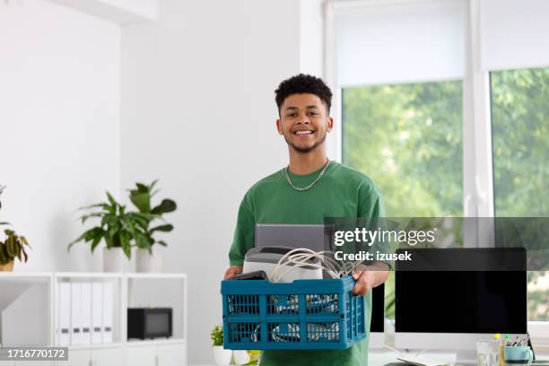portrait of smiling young businessman carrying container at office - man holding donation box stock pictures, royalty-free photos & images