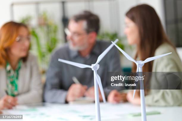 windradmodelle gegen kollegen, die im büro diskutieren - grünes wirtschaften stock-fotos und bilder