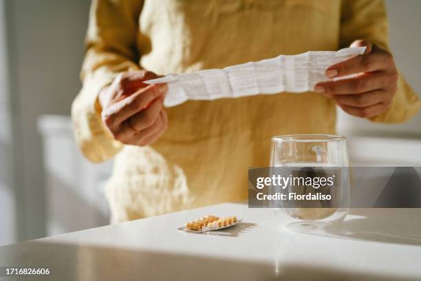 a woman standing at a table with green pills in her hand - comprimés photos et images de collection
